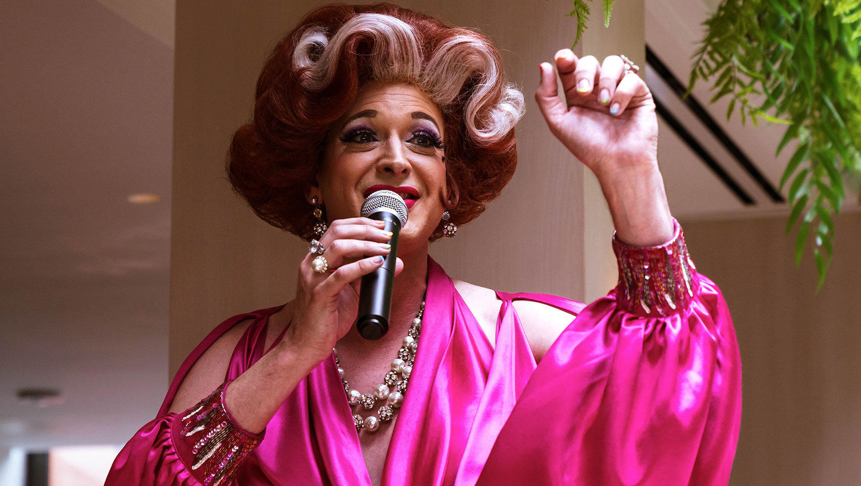 Drag queen in pink dress with lots of jewelry with microphone