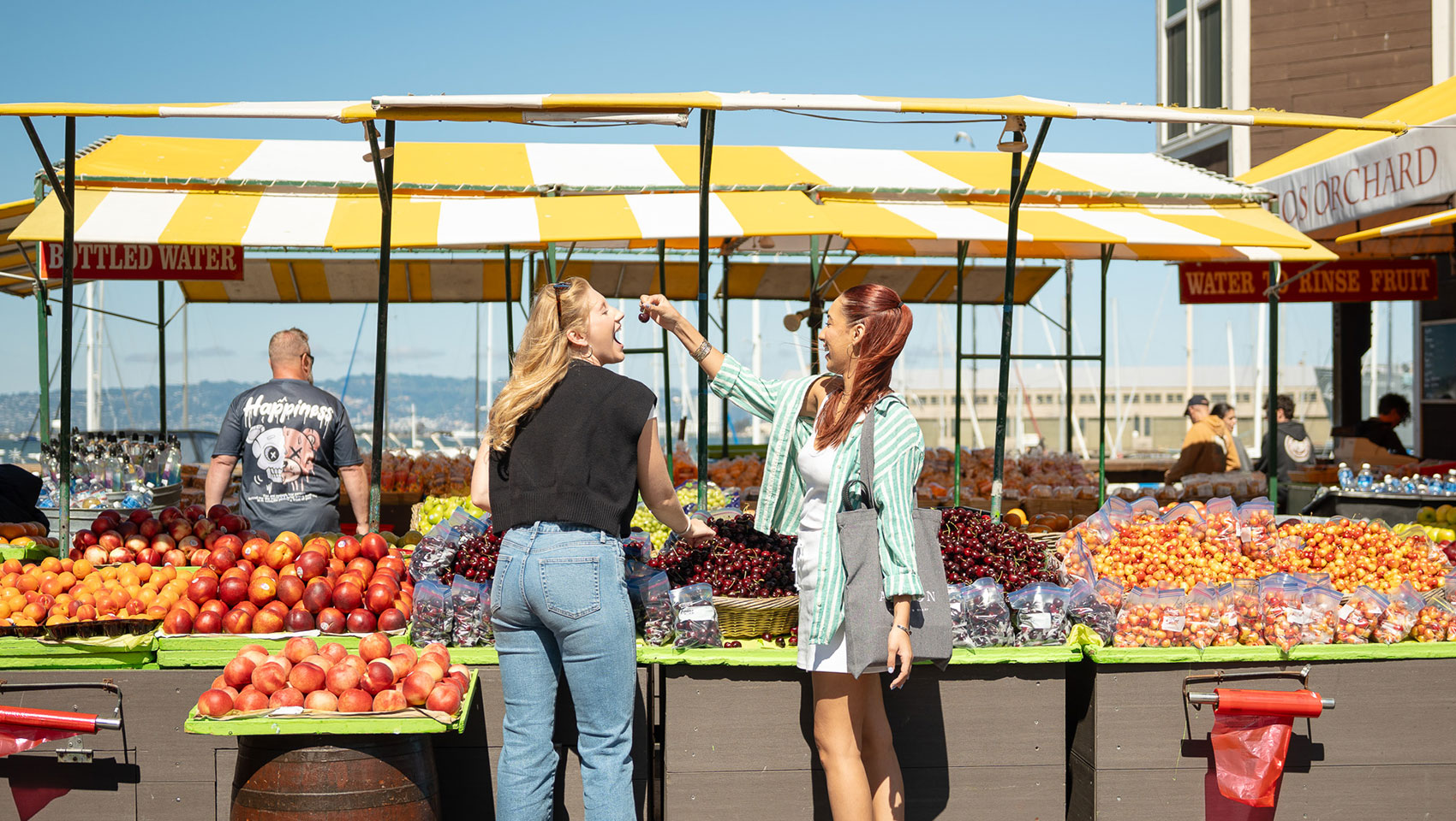 2 women sample fruit at a san francisco farmers market