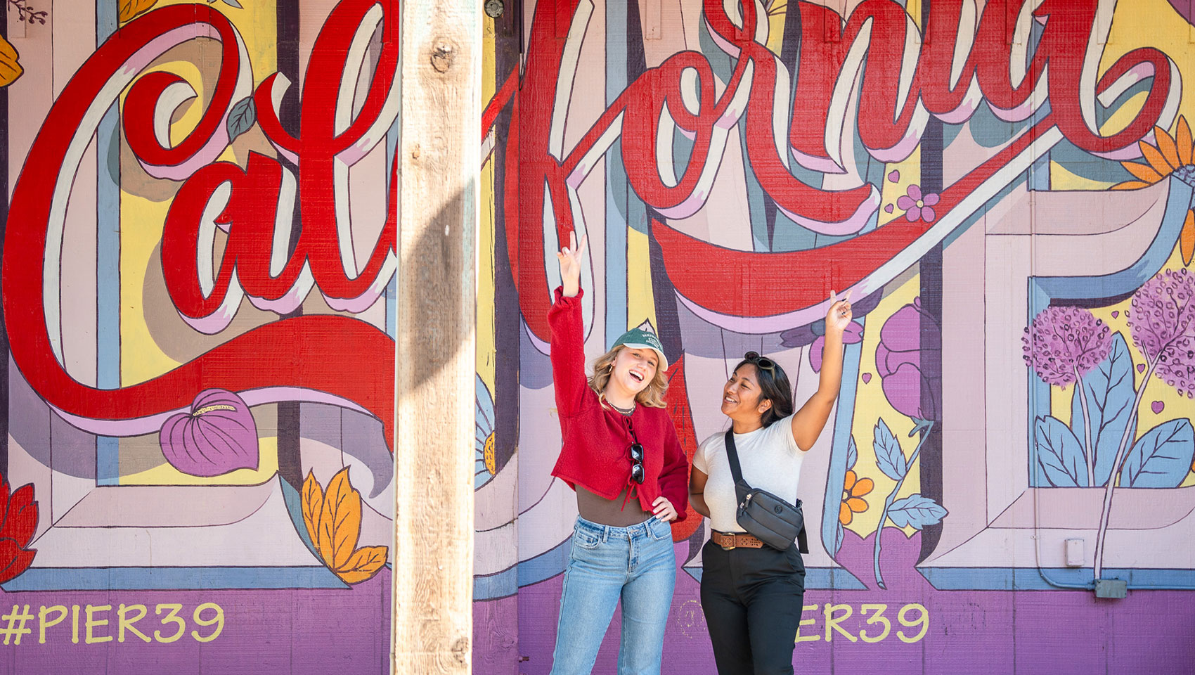 2 women pose in front of mural