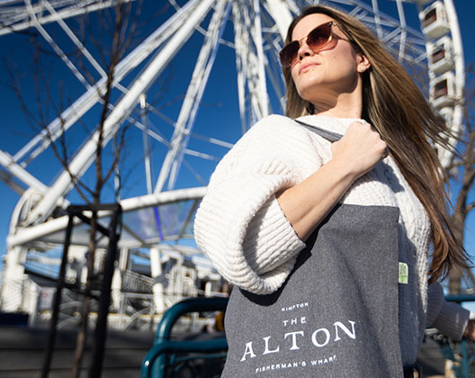 Woman stands in front of SkyStar Wheel Ferris Wheel holding an Alton tote bag