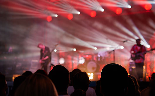 Silhouettes of crowd at concert in front of stage with bright spotlights